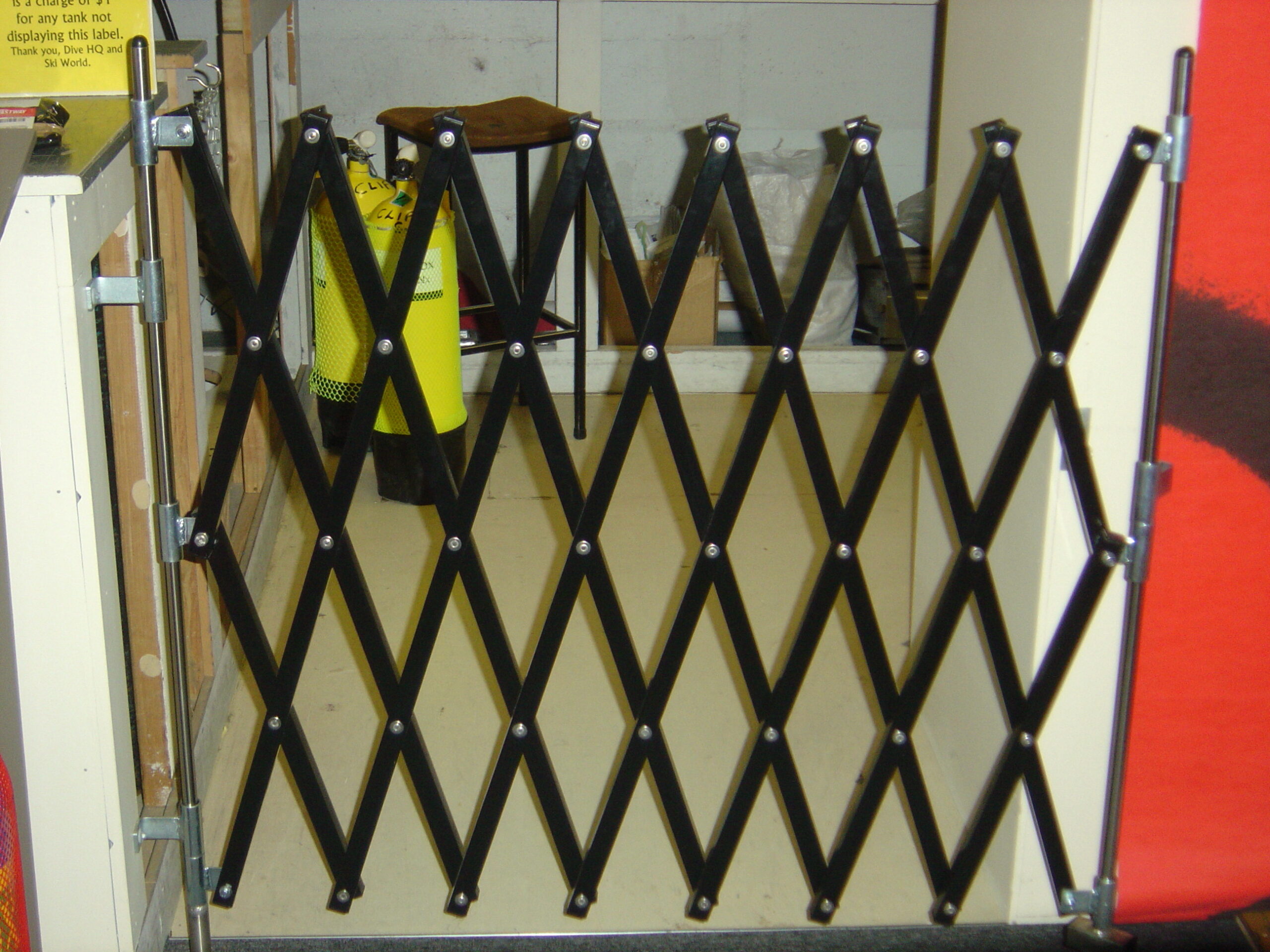 A black XPANDO portable barrier by E S Barriers used as a security gate in an indoor setting.