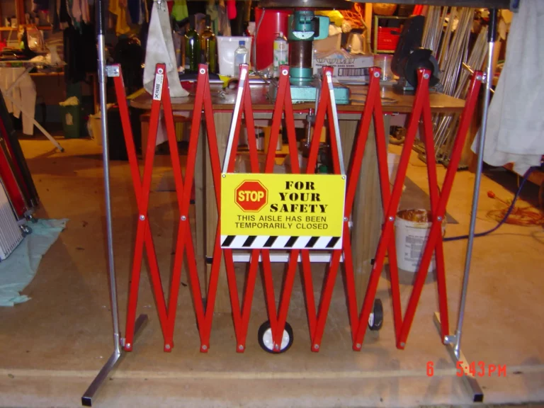 A red XPANDO barrier by E S Barriers featuring a safety sign for restricted access in a workshop or warehouse setting.